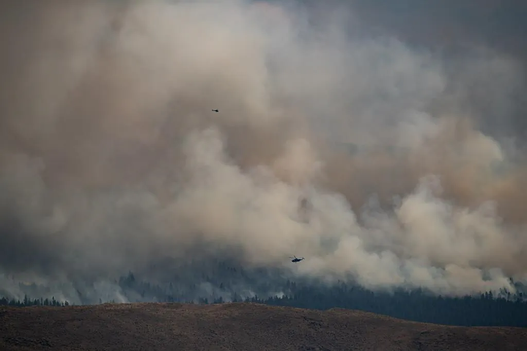 Helicopters fly past the Tremont Creek wildfire as it burns on the mountains above Ashcroft, B.C., on July 16, 2021. (The Canadian Press/Darryl Dyck)