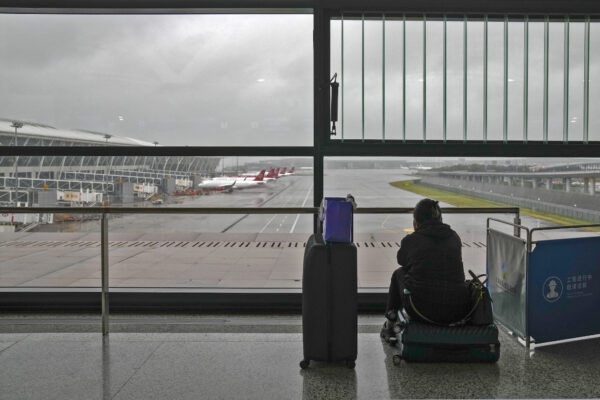 A passenger sits on her luggage watching the passenger airplanes
