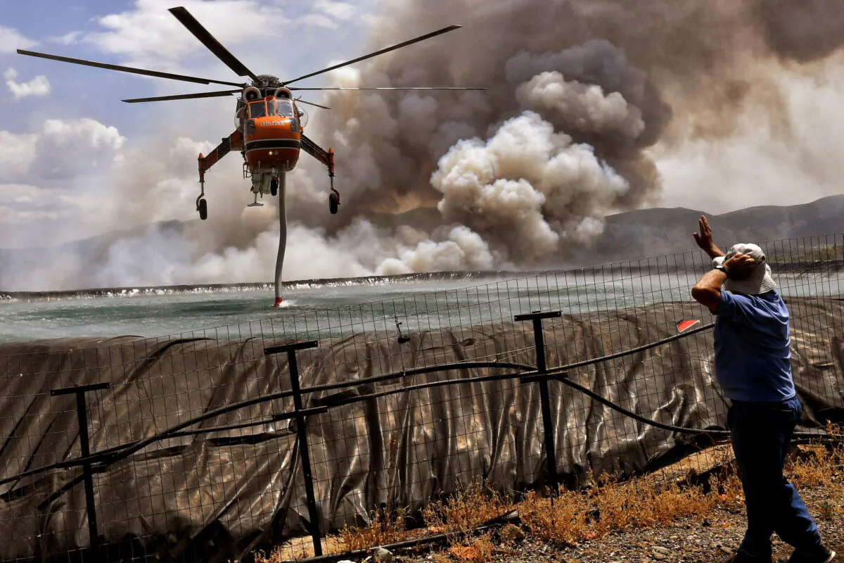 A helicopter is being filled up with water from a tank as a wildfire burns near the village of Spathovouni, near Corinth, Greece, on July 23, 2021. (Vassilis Psomas/Reuters)