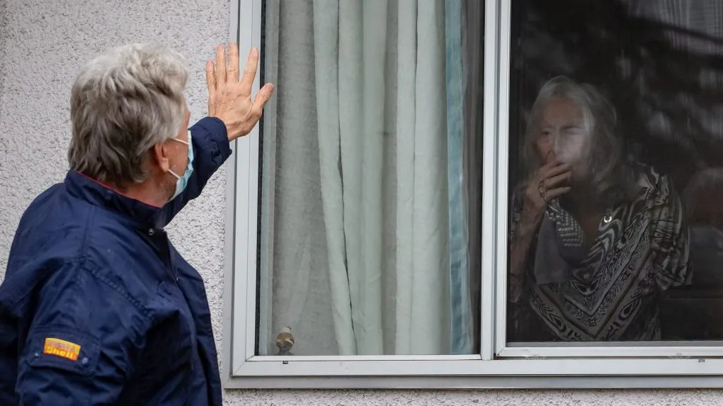 A man waves to his mother from the window of her room at Tabor Home, a long-term care facility in Abbotsford, B.C., on Nov. 18, 2020. (The Canadian Press/Darryl Dyck) 