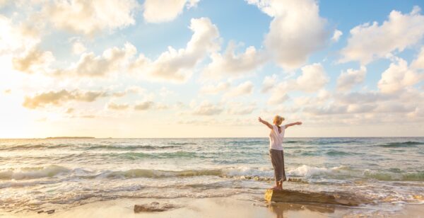 a woman stands with her arms wide at the shore of the ocean