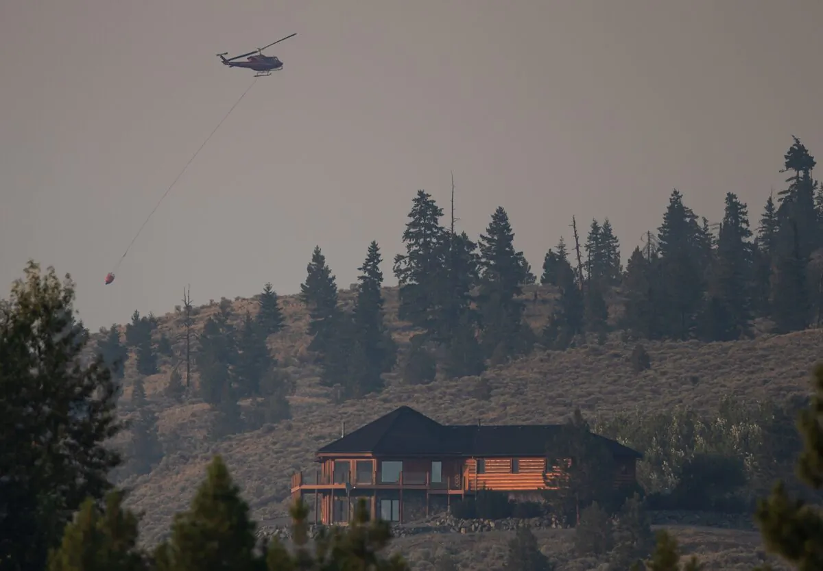 A helicopter carrying a bucket flies over a property in Barnes Lake while battling the Tremont Creek wildfire near Ashcroft, B.C., on July 15, 2021. (The Canadian Press/Darryl Dyck)