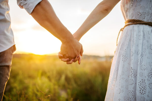 Couple,Hold,Hands,In,Green,Field,On,Sunset