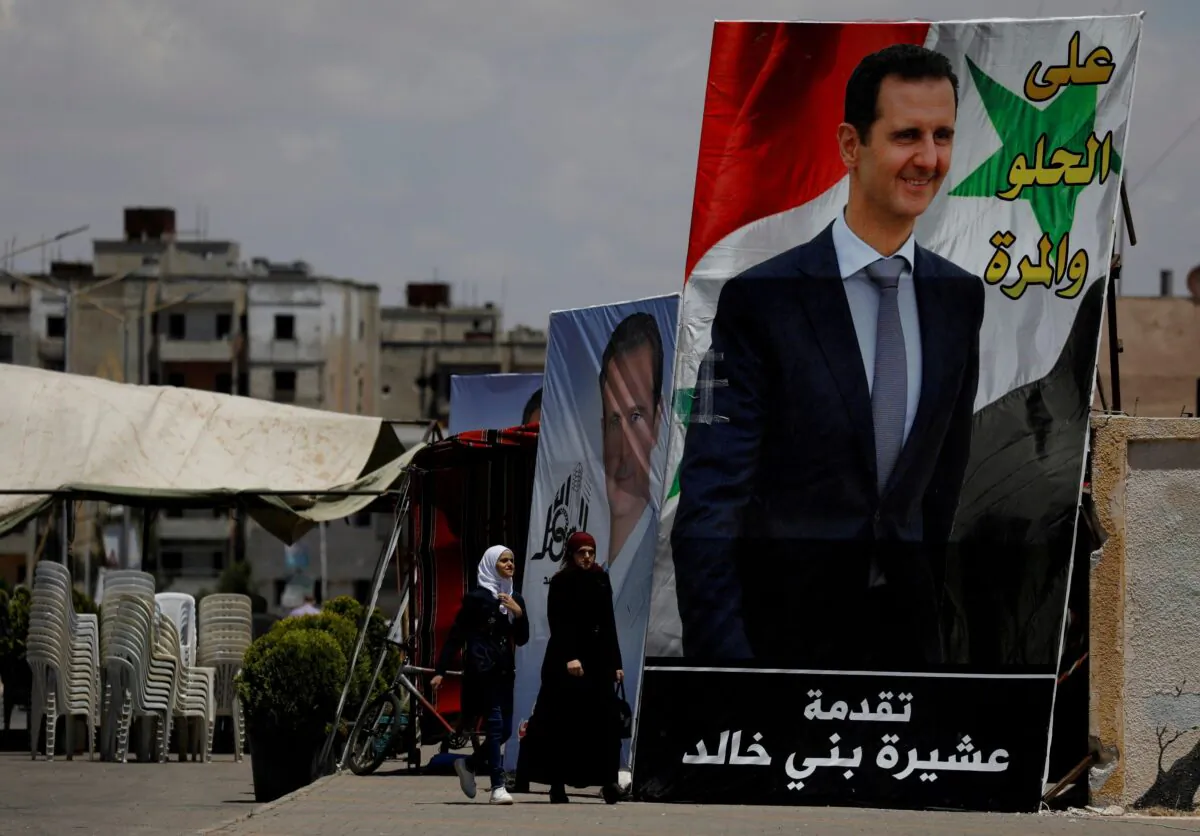 People walk past posters depciting Syria's President Bashar al-Assad, ahead of the May 26 presidential election, in the district of al-Waer in Homs, Syria, on May 23, 2021. (Omar Sanadiki/Reuters)