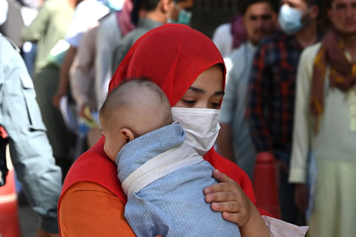 A woman with a child stands in a queue along with others to submit their passport applications at an office in Kabul on July 25, 2021. (Sajjad Hussain/AFP via Getty Images)