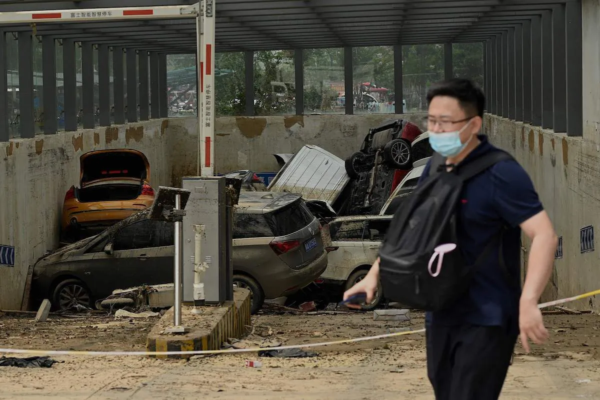 A man on July 24, 2021, walks past a car park with damaged vehicles stacked on each other following heavy rain which caused flooding days earlier that claimed at least 56 lives, in the city of Zhengzhou in China's Henan Province. (Noel Celis/AFP via Getty Images)
