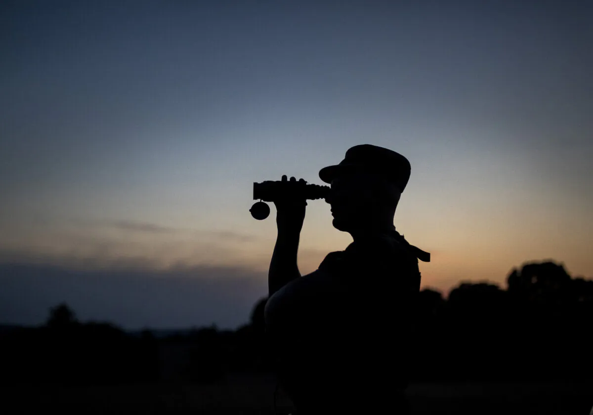 A member of the Lithuania State Border Guard Service looks through binoculars as he patrols on the border with Belarus, near the village of Purvenai, Lithuania, on July 9, 2021.  (Mindaugas Kulbis/AP Photo)