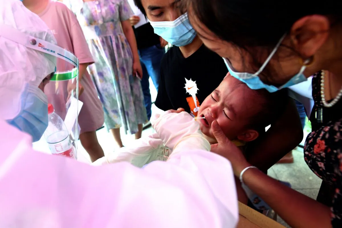 A medical worker takes swab samples from a child during mass testing for the CCP virus at a residential block in Wuhan, Hubei province, China, on Aug. 3, 2021. (Chinatopix via AP)