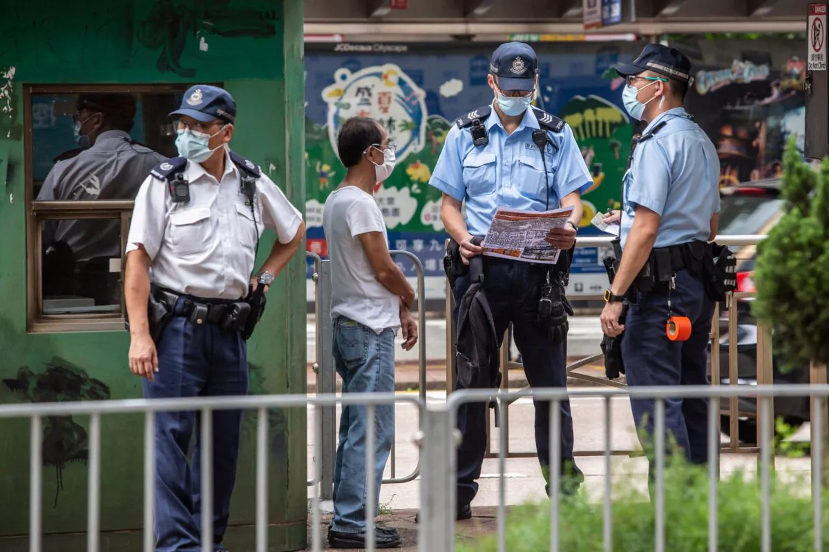 A police officer (centre R) reads a leaflet found during a stop and search on a man (2nd L) outside the High Court in Hong Kong on July 30, 2021, after Tong Ying-kit was sentenced to nine years in prison for terrorism and inciting secession in the first trial conducted under a national security law imposed by China. (Isaac Lawrence/AFP via Getty Images)