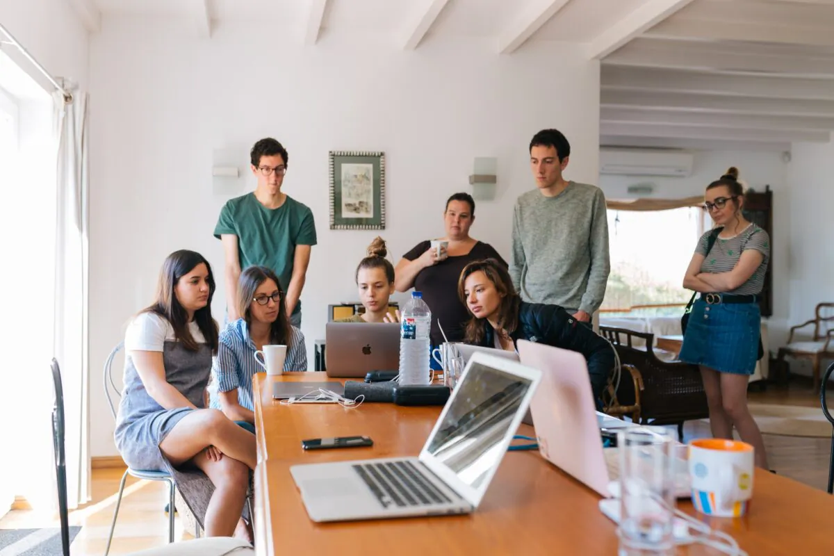 Company employees gather together around a laptop. (Pexels)