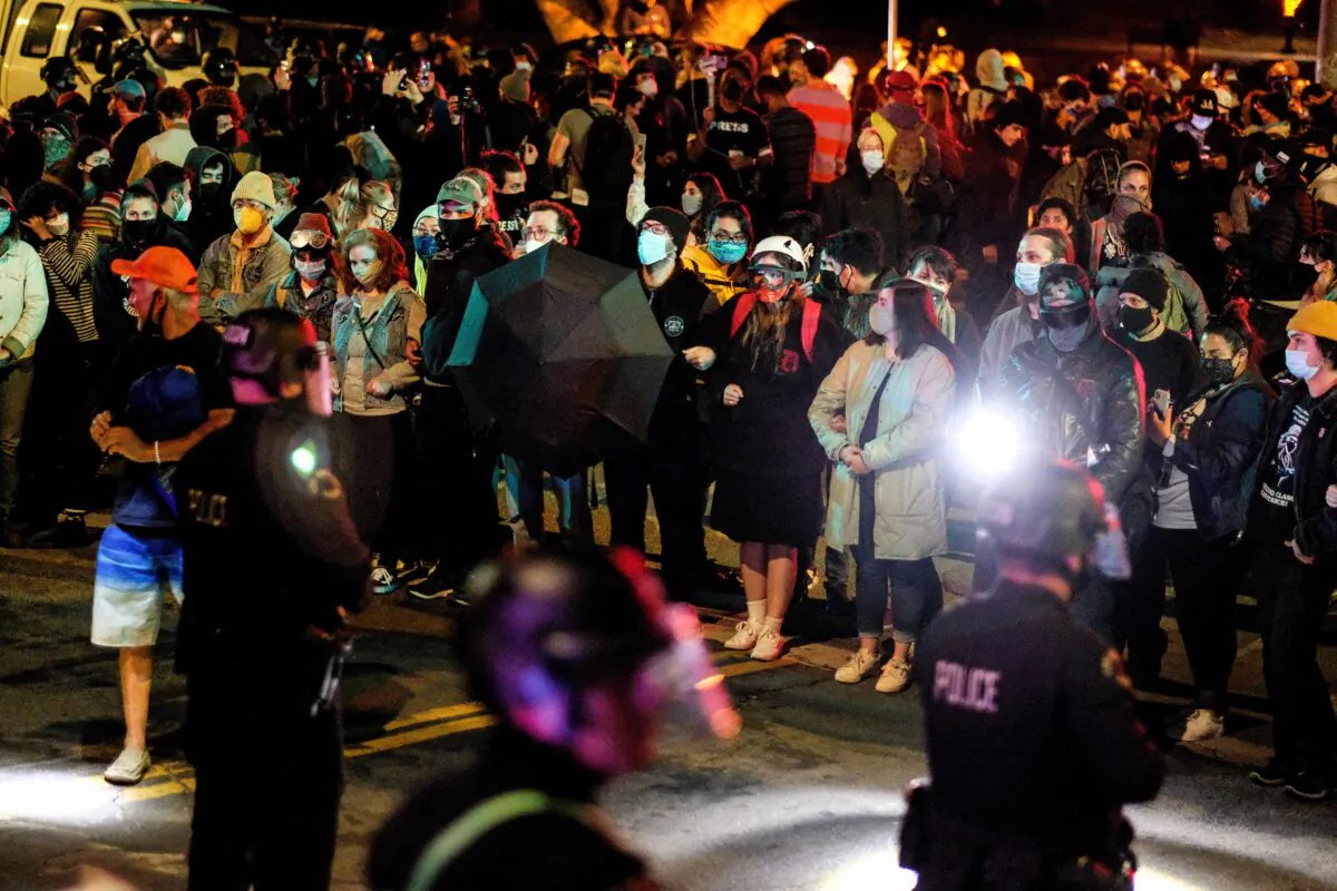Activists and supporters of residents of a homeless encampment protest in front of police at Echo Park Lake in Los Angeles late on March 24, 2021, ahead of a planned and announced clean-up of the encampment. (Photo by RINGO CHIU/AFP via Getty Images)