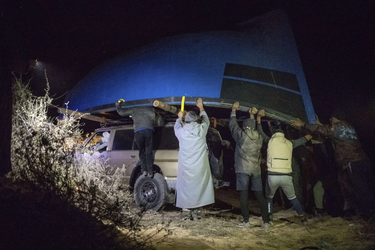 Smugglers lift onto a vehicle a fishing boat intended to be used to transport migrants to the Canary Islands, in a remote desert out of the town of Dakhla in Morocco-administered Western Sahara, on Dec. 22, 2020. (Mosa'ab Elshamy/AP Photo)