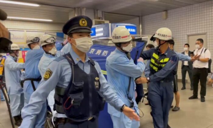 Police escort rescue workers carrying a person through a train station after a knife attack on a train in Tokyo, in this still image taken from video, Japan, on Aug. 6, 2021. (Reuters)