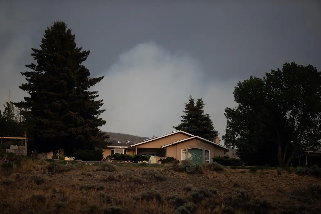 Smoke from the Tremont Creek wildfire burning on a mountain rises in the distance behind a home in Ashcroft, B.C., on July 15, 2021. British Columbia’s wildfire danger map shows a low to moderate fire risk over much of the province after a rainy weekend, but the extreme risk is expected to resume quickly as another hot spell arrives. (The Canadian Press/Darryl Dyck)