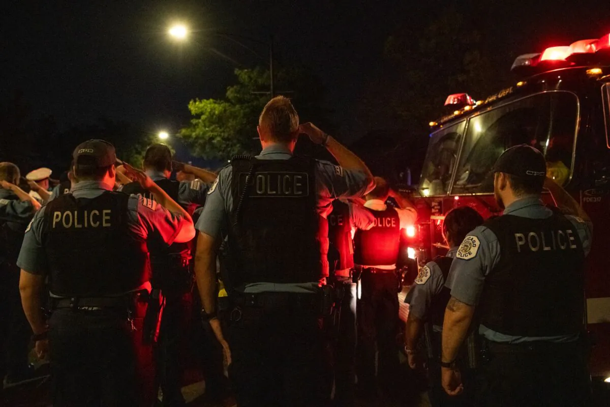 Police officers salute as a procession for a police officer who was shot and killed earlier during a traffic stop at 63rd and Bell drives by the Cook County Medical Examiners Office, in Chicago, on Aug. 8, 2021. (Tyler LaRiviere/Chicago Sun-Times via AP)