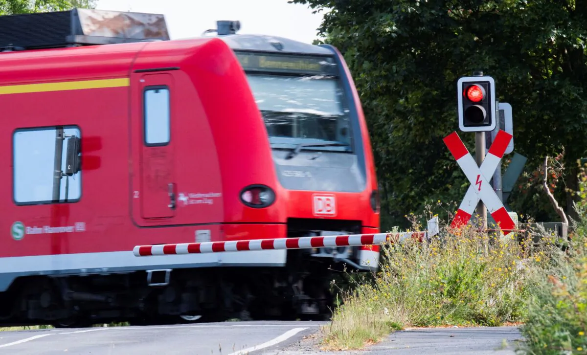 A Deutsche Bahn (DB) commuter train passes a level crossing with a red light in Roessing, Germany, on Aug. 11, 2021. (Julian Stratenschulte/dpa via AP)
