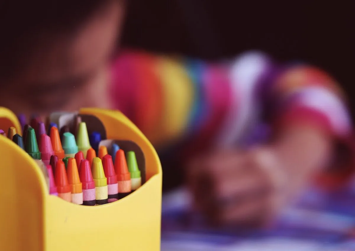 Stock photo of a child sitting near crayons. (Aaron Burden/Unsplash)