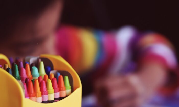 Stock photo of a child sitting near crayons. (Aaron Burden/Unsplash)