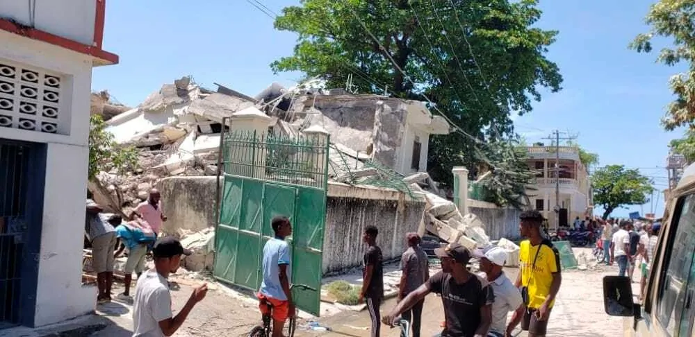 People stand outside the residence of the Catholic bishop after it was damaged by an earthquake in Les Cayes, Haiti, on Aug. 14, 2021. (The Canadian Press/AP-Delot Jean)