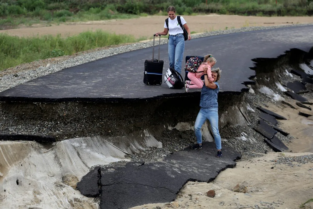 Tourists try to walk along a road damaged by flooding near the village of Tsybanobalka, Krasnodar region, Russia, on Aug. 14, 2021. (AP Photo)
