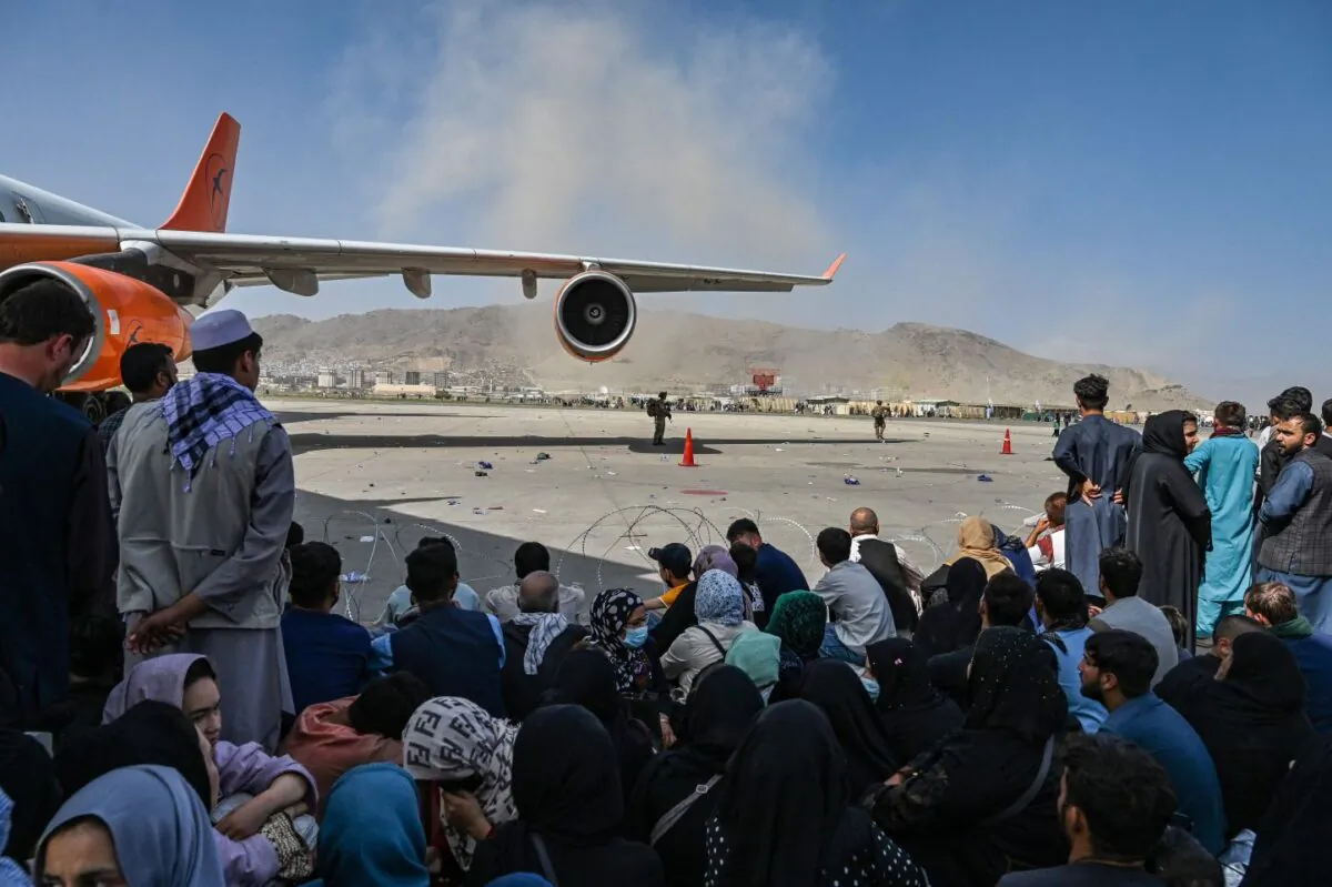 Afghan people sit as they wait to leave the Kabul airport after a stunningly swift end to Afghanistan's 20-year war, in Kabul on Aug. 16, 2021. (Wakil Kohsar/AFP via Getty Images)