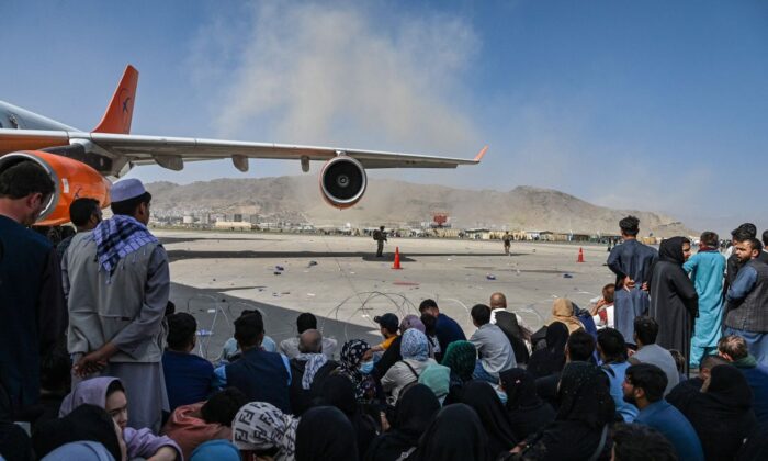 Afghan people sit as they wait to leave the Kabul airport after a stunningly swift end to Afghanistan's 20-year war, in Kabul on Aug. 16, 2021. (Wakil Kohsar/AFP via Getty Images)