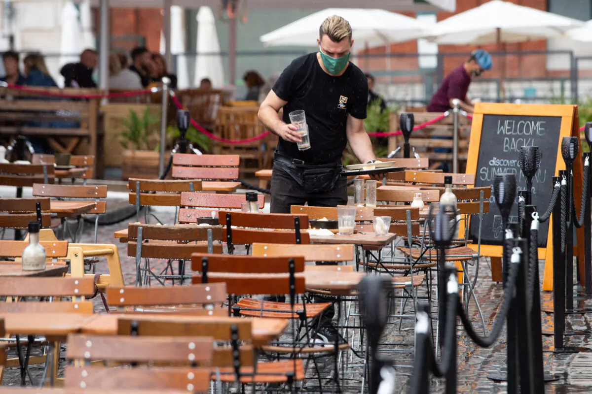 A waiters clears empty outside tables following a downpour of rain in Covent Garden, London, on July 4, 2021. (Dominic Lipinski/PA)