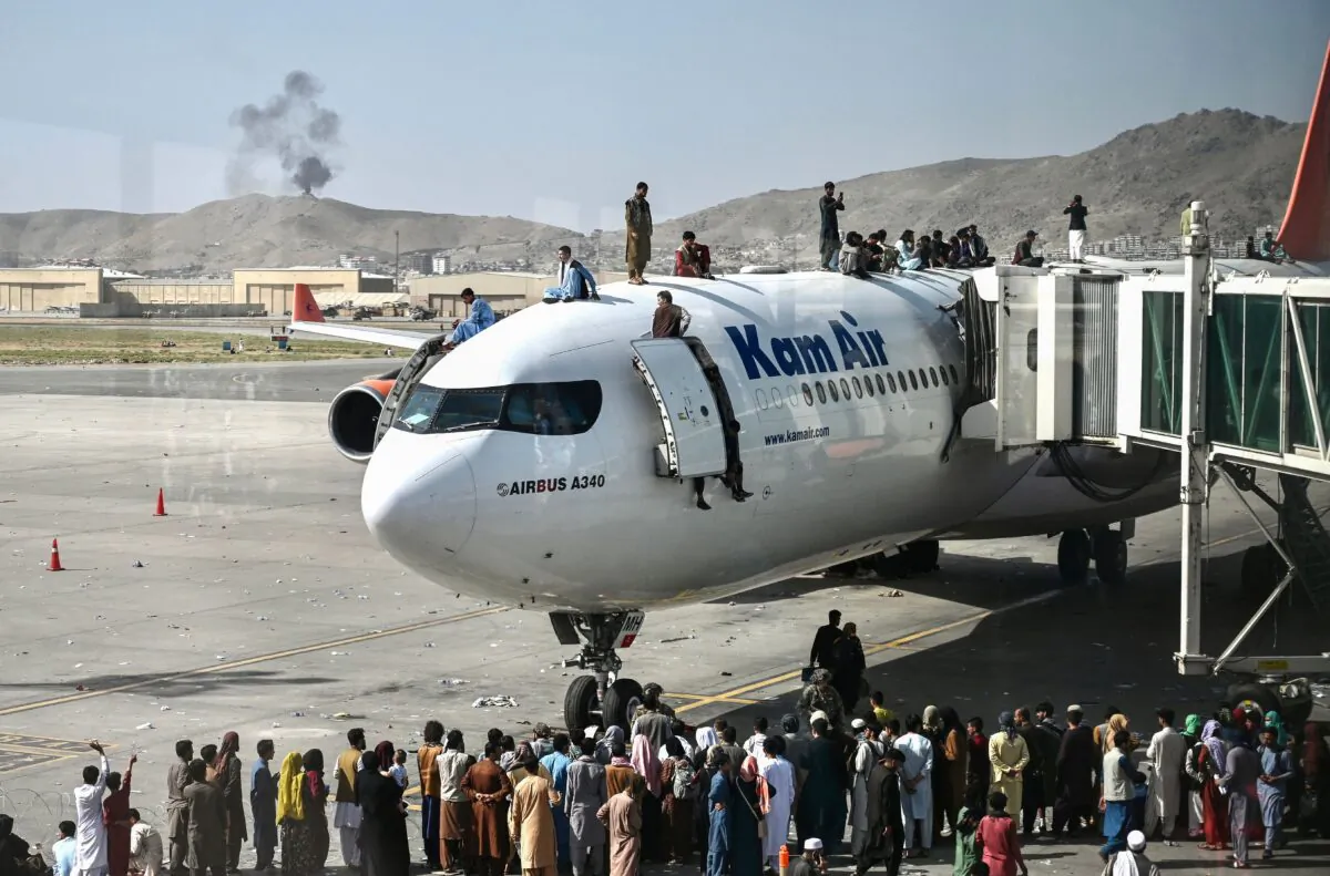 Afghan people climb atop a plane as they wait at the Kabul airport in Kabul on Aug. 16, 2021. (Wakil Kohsar/AFP via Getty Images)