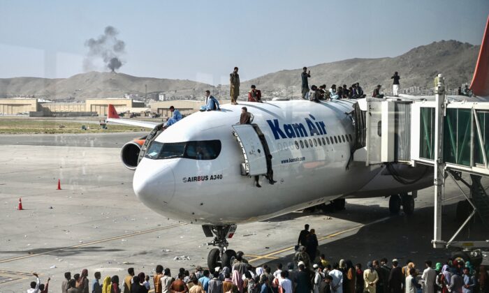 Afghan people climb atop a plane as they wait at the Kabul airport in Kabul, Afghanistan, on Aug. 16, 2021. (Wakil Kohsar/AFP via Getty Images)