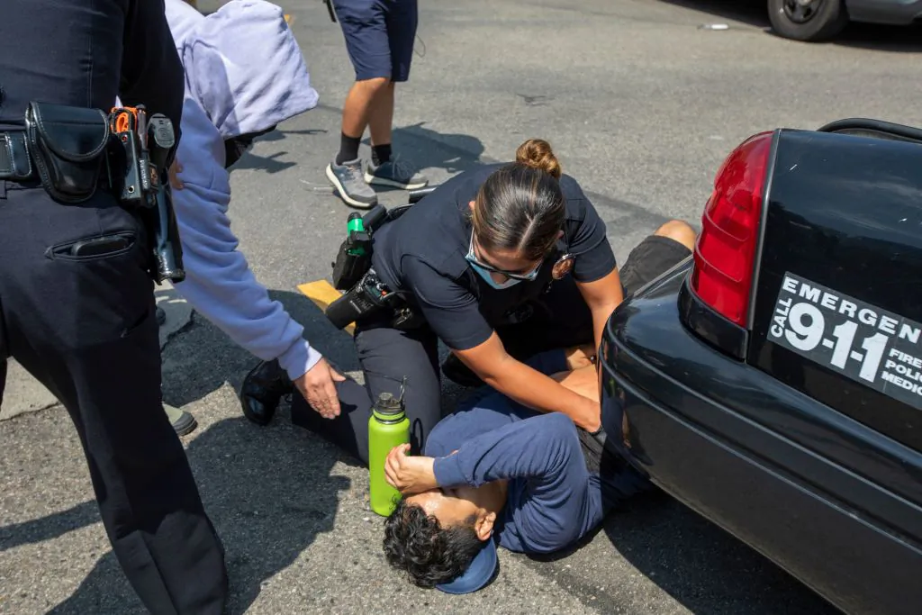 A police officer assists a man who was stabbed during a rally near City Hall in Los Angeles on August 14, 2021. (David McNew/AFP via Getty Images)