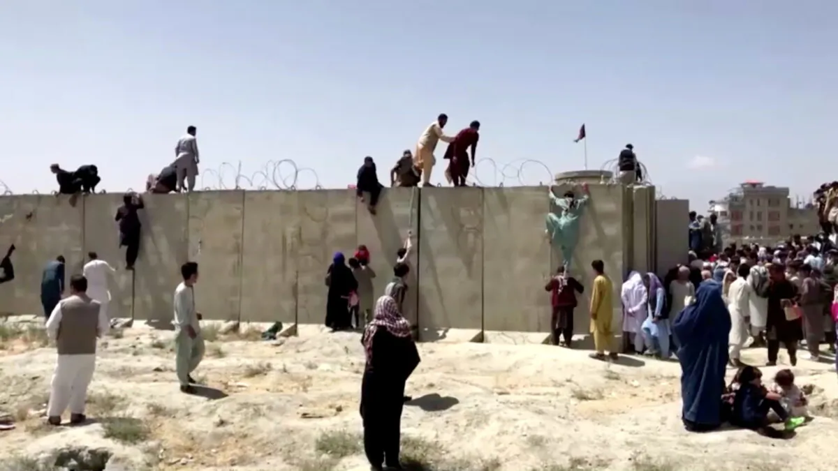 People climb a barbed wire wall to enter the airport in Kabul, Afghanistan August 16, 2021, in this still image taken from a video. (Reuters TV/via Reuters)