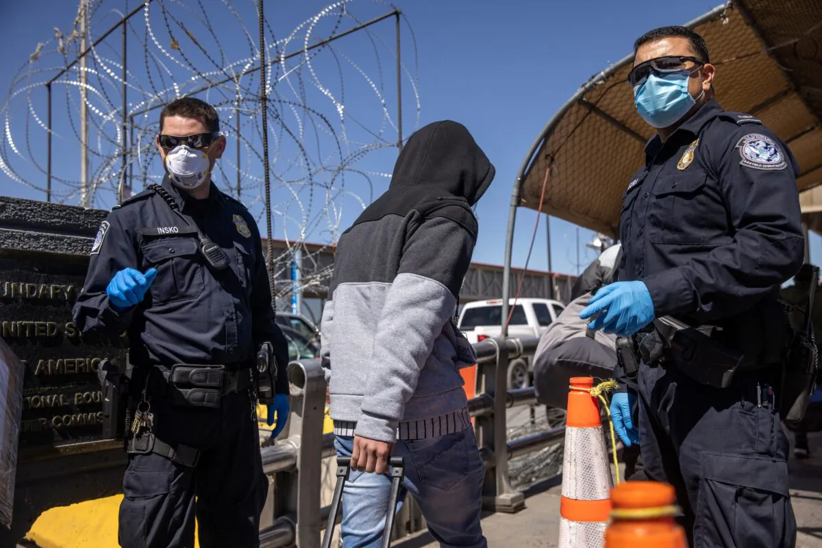 Asylum seekers pass U.S. Customs and Border Protection officers while crossing an international bridge from Mexico into the United States in Ciudad Juarez, Mexico, on March 17, 2021. (John Moore/Getty Images)