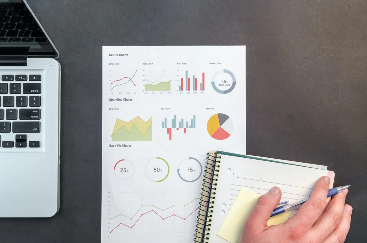 Photo of laptop, paper with graphs and a handwritten notepad. (Lukas/Pexels)