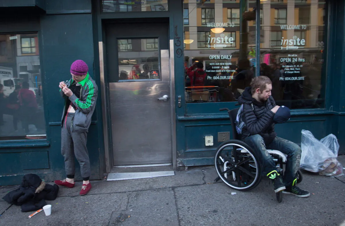 A woman prepares to inject herself with an unknown substance as a man sits in a wheelchair outside the Insite supervised consumption facility in Vancouver’s Downtown Eastside on Feb. 21, 2017. (The Canadian Press/Darryl Dyck)