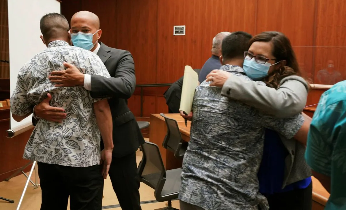 Defense attorney Thomas Otake, (L) facing camera, embraces Geoffrey Thom, as defense attorney Crystal Glendon, (R) facing camera, embraces her client Christopher Fredeluces after Judge William Domingo rejected murder and attempted murder charges against the officers in the fatal shooting of a teenager, preventing the case from going to trial, at district court in Honolulu, Hawaii, on Aug. 18, 2021. (Cory Lum/Pool/Honolulu Civil Beat via AP)