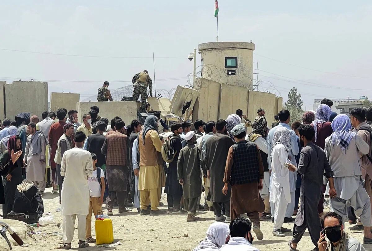 Afghan security guards stand on a wall as hundreds of people gather outside the international airport in Kabul, Afghanistan, on Aug. 17, 2021. (AP Photo)
