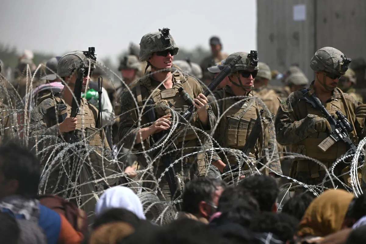 U.S. soldiers stand guard behind barbed wire as Afghans sit on a roadside near the military part of the airport in Kabul, Afghanistan on Aug. 20, 2021. (Wakil Kohsar/AFP via Getty Images)