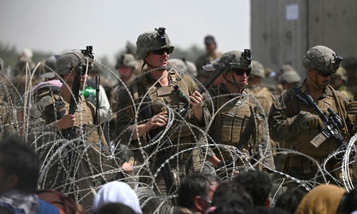 U.S. soldiers stand guard behind barbed wire as Afghans sit on a roadside near the military part of the airport in Kabul, Afghanistan on Aug. 20, 2021. (Wakil Kohsar/AFP via Getty Images)