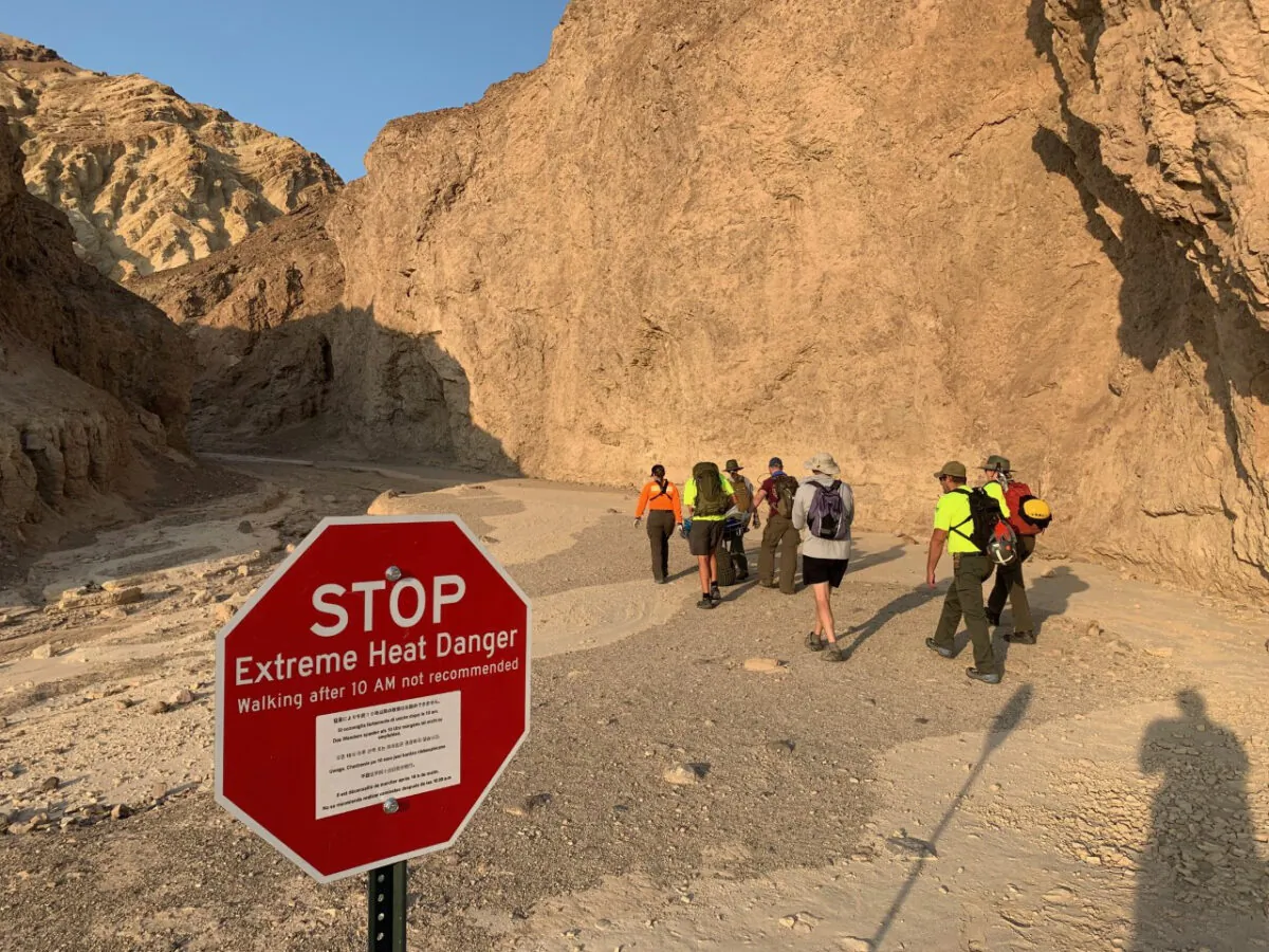 An inter-agency search and rescue crew walks past a sign reading" "Stop, Extreme Heat Danger," with park rangers responding on foot near Red Cathedral along the Golden Canyon Trail in Death Valley National Park, Calif., on Aug. 18, 2021. (National Park Service via AP)