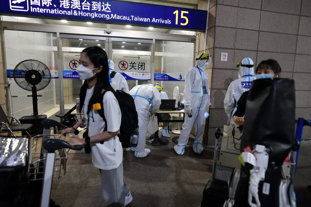 Pudong airport workers in protective clothing help arriving international passengers as they prepare to board buses to be taken to quarantine hotels in Shanghai on Aug. 13, 2021. (Greg Baker/AFP)