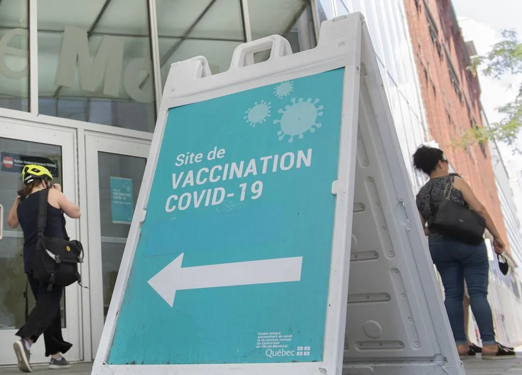 People are shown next to a COVID-19 vaccination sign in Montreal, on Aug. 21, 2021. (The Canadian Press/Graham Hughes)