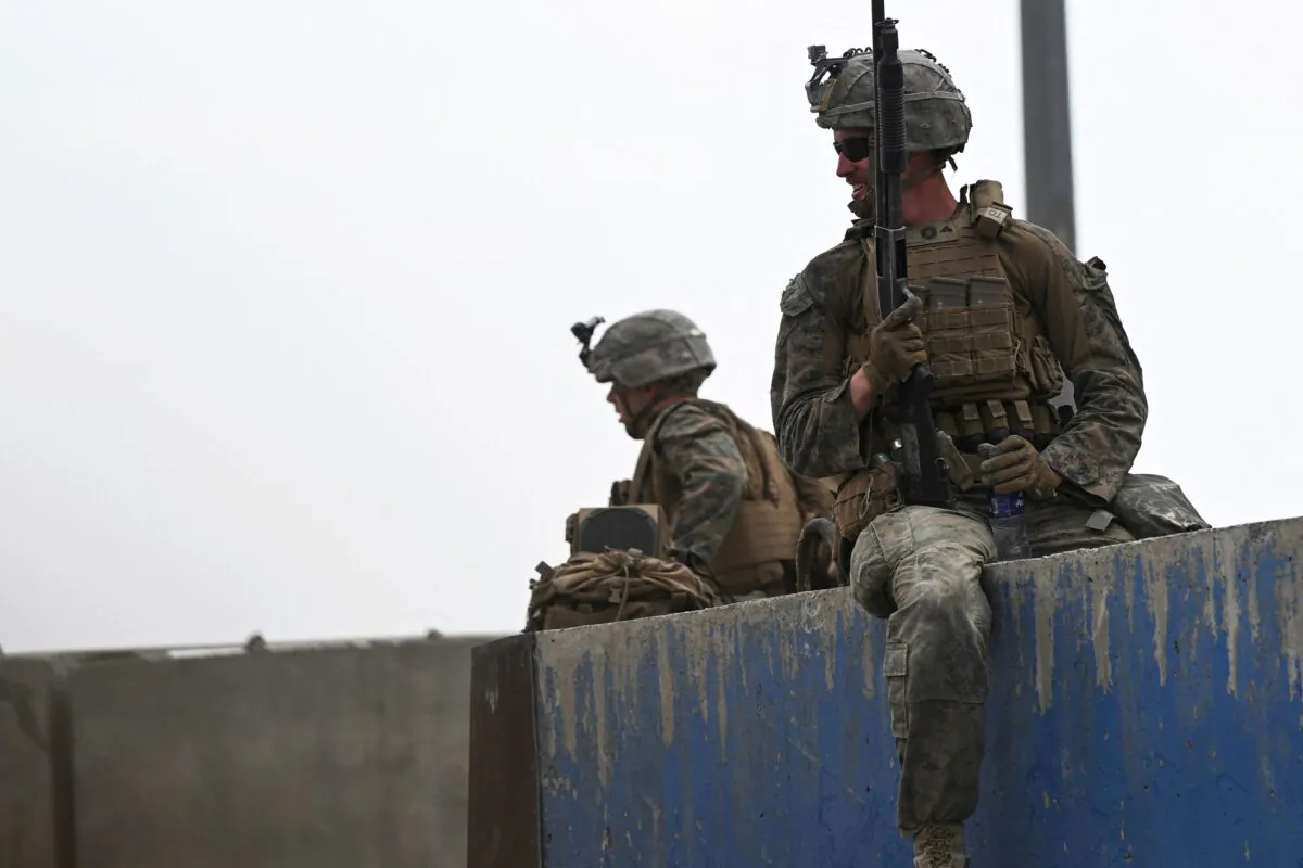 U.S. soldiers sit on a wall as Afghans gather on a roadside near the military part of the airport in Kabul on Aug. 20, 2021. (Wakil Kohsar/AFP)