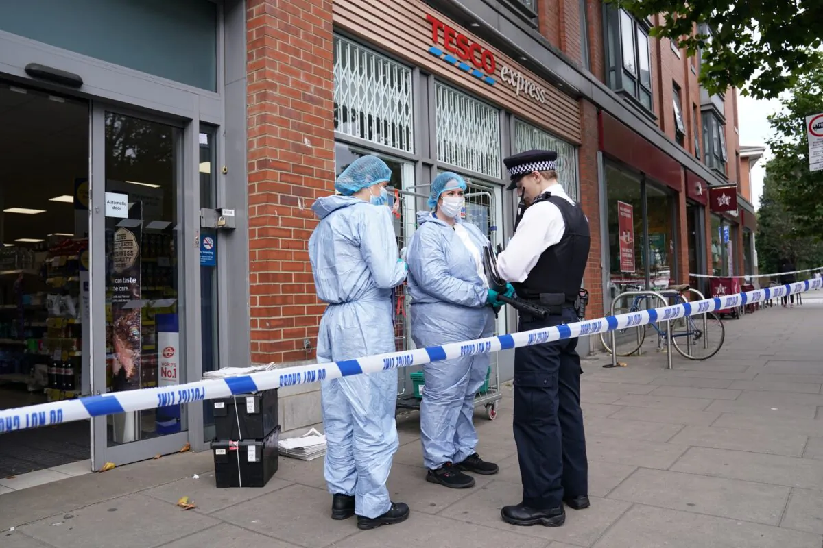 In this file image police officers in forensic suits speak to a colleague outside Tesco Express on Fulham Palace Road, in west London, UK, on Aug. 26, 2021. (Jonathan Brady/PA)