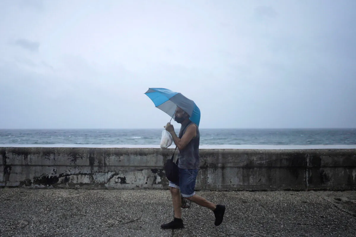 A man protects himself from wind and rain as he walks at the seafront Malecon while Hurricane Ida approaches the island, in Havana, Cuba, on Aug. 27, 2021. (Alexandre Meneghini/Reuters)