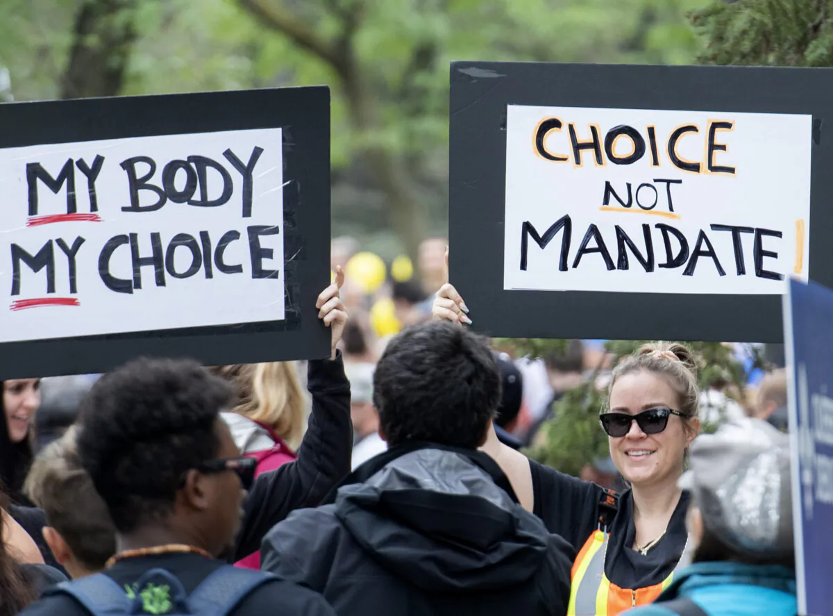 People hold signs during a demonstration opposing the Quebec government’s COVID-19 vaccination passport system, in Montreal on Aug. 28, 2021. (The Canadian Press/Graham Hughes)