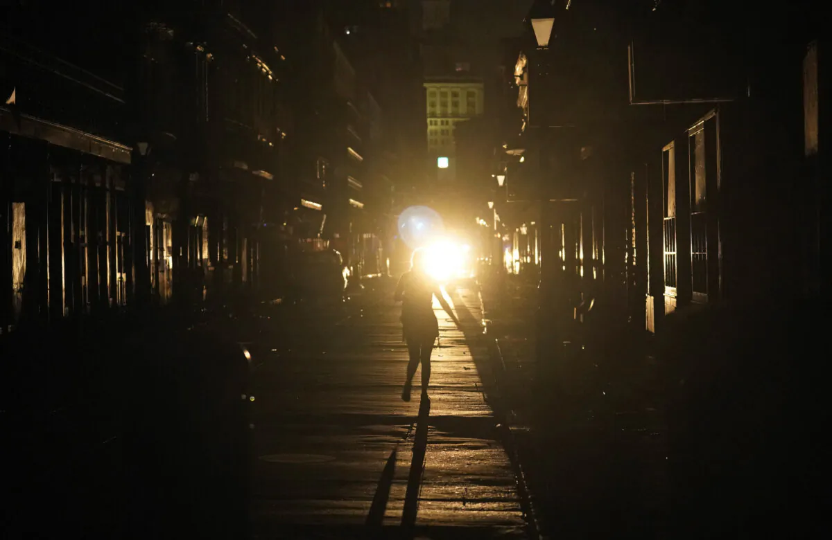 A police officer patrols past woman walking along Bourbon Street in the French Quarter after Hurricane Ida knocked out power to the city, in New Orleans, La., on Aug. 30, 2021. (Eric Gay/AP Photo)