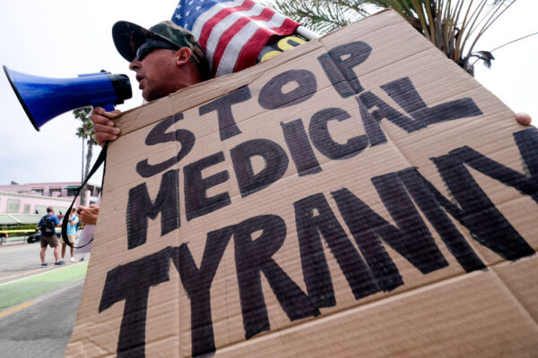 A protester holds a sign and a flag as he takes part in a rally against COVID-19 vaccine mandates, in Santa Monica, Calif., on Aug. 29, 2021. (Ringo Chiu/AFP via Getty Images)
