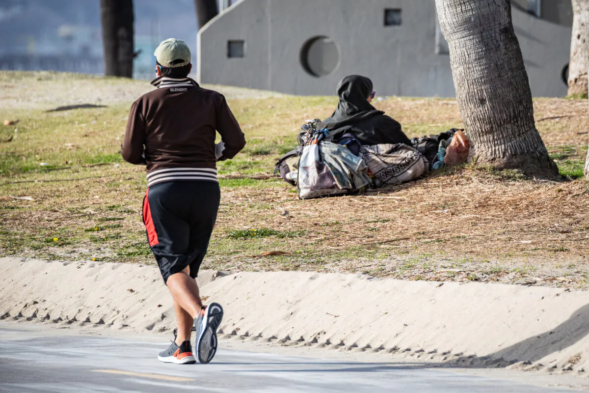 A jogger runs past a homeless man in Venice Beach, Calif., on Jan. 27, 2021. (John Fredricks/The Epoch Times)