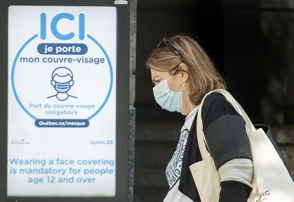 A woman wears a face mask as she walks by a sign advising of the mandatory wearing of masks and face coverings in Montreal on Sept. 21, 2020. (The Canadian Press/Graham Hughes)