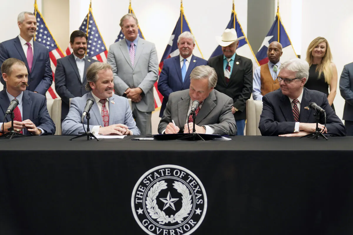 Texas Gov Greg Abbott signs Senate Bill 1, also known as the election integrity bill, into law with State Sen. Bryan Hughes ( R-Mineola), front center left, Andrew Murr (R-Junction),  front left, and Lieutenant Governor Dan Patrick, front right, looking on with others in the back ground in Tyler, Texas, on Sept. 7, 2021. (LM Otero/AP Photo)